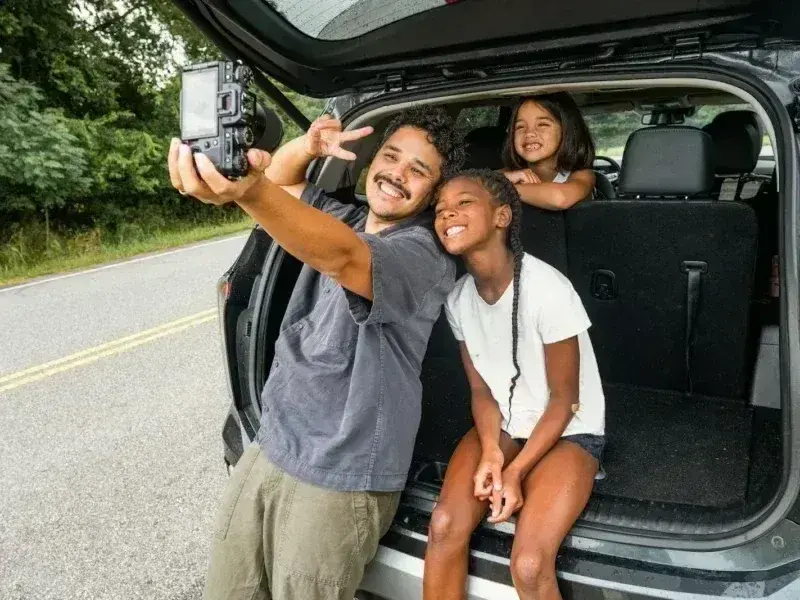Father and daughters take a selfie by the car.