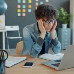 A person looking stressed at a laptop in an office.